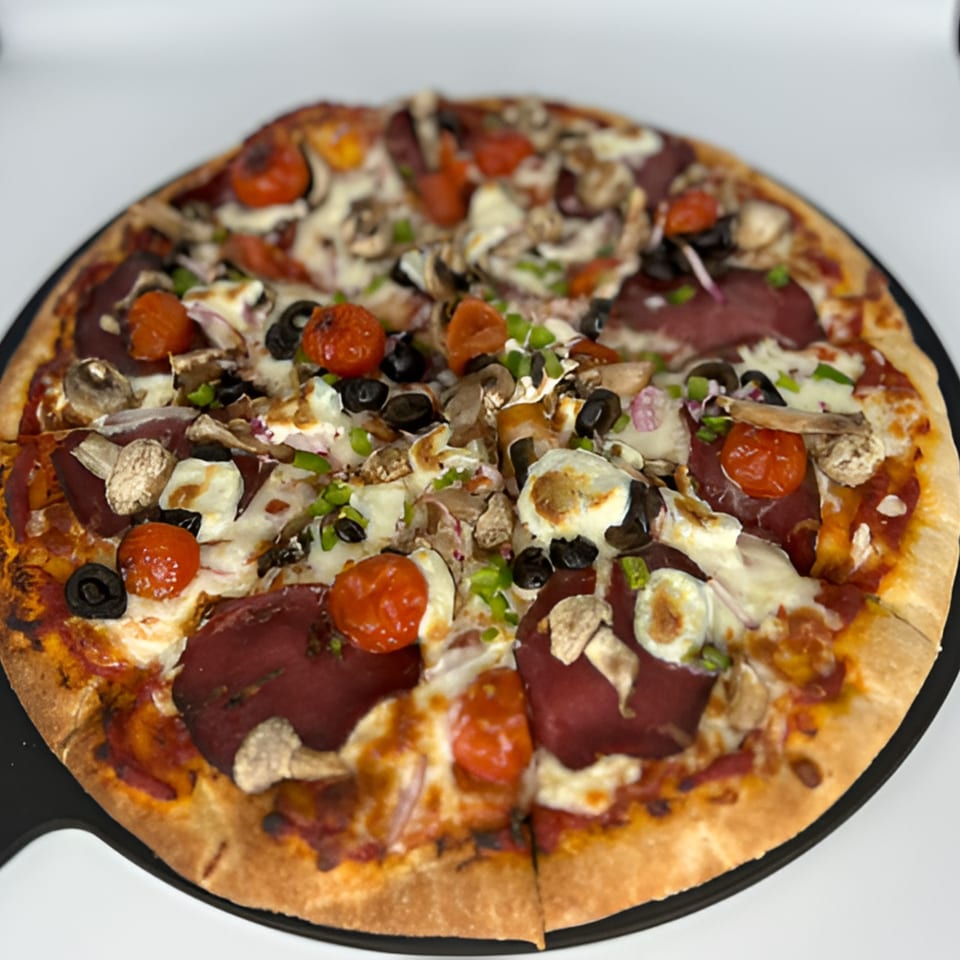 Tito's Lounge pizza with salami, cherry tomatoes, mushrooms, olives, and cheese on a black tray.