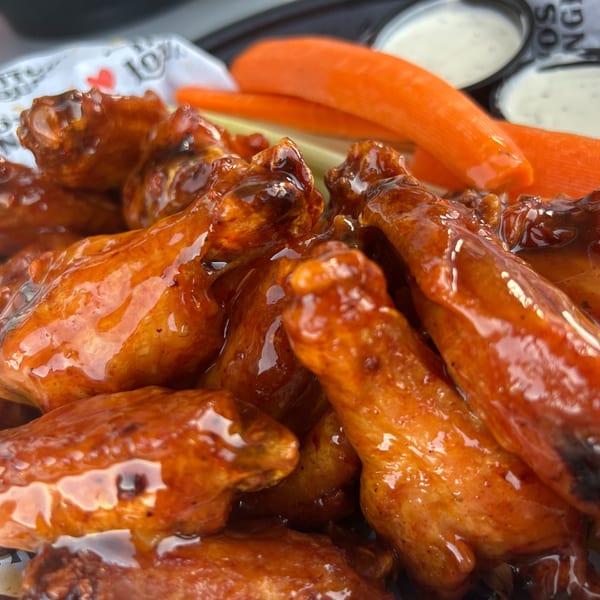 Close-up of Tito's Lounge's glazed chicken wings with carrots, celery, and dipping sauces.
