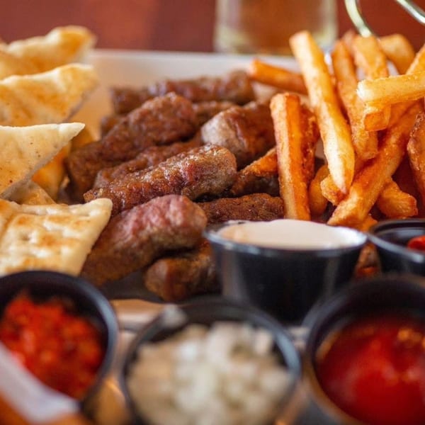 Tito's Lounge cevapi with fries, pita bread, and three dipping sauces.