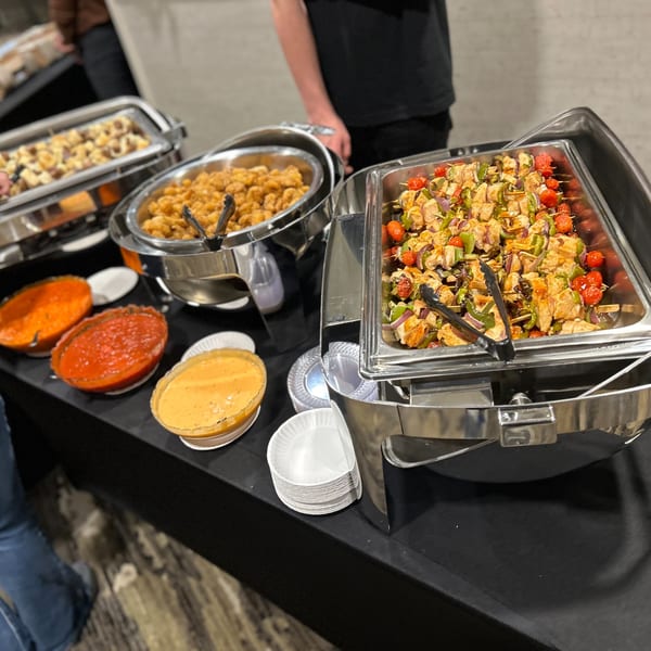 A buffet spread with chafing dishes of chicken skewers, fried food, and bowls of sauces.