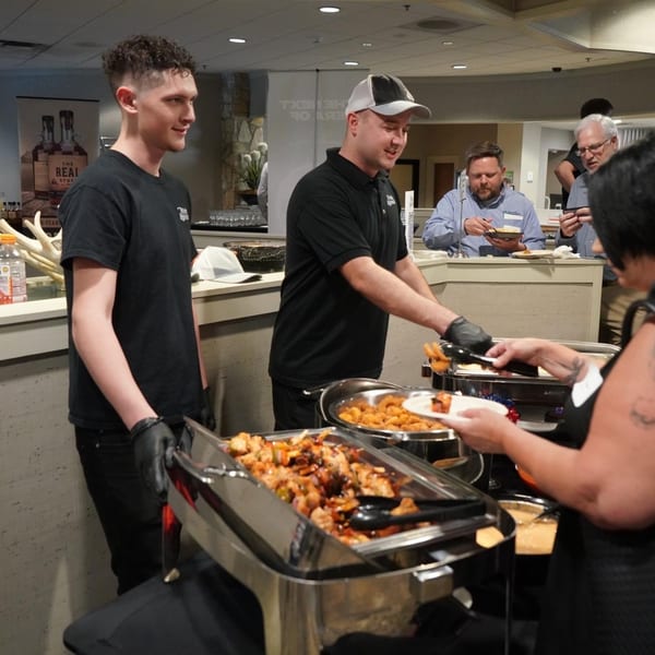 Tito's Lounge staff serving food from chafing dishes to customers at a buffet line.