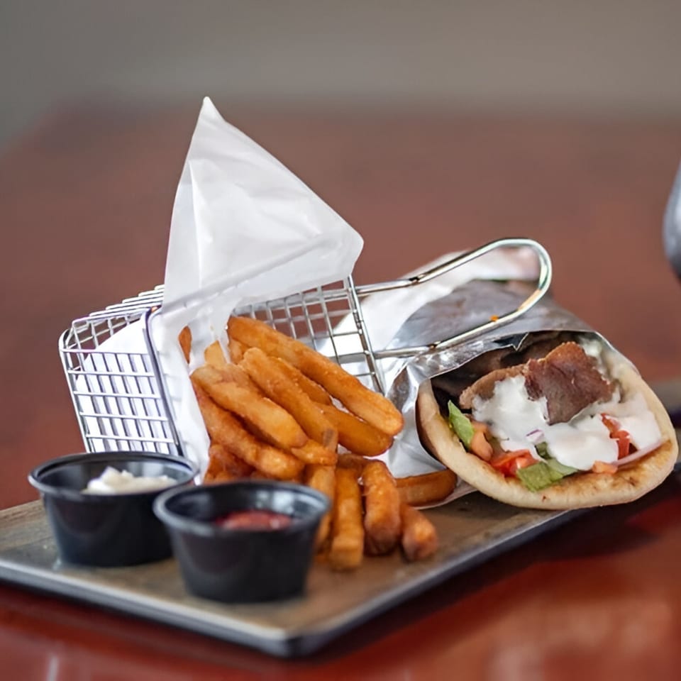 A Tito's Lounge gyro with fries and dipping sauces on a metal tray.