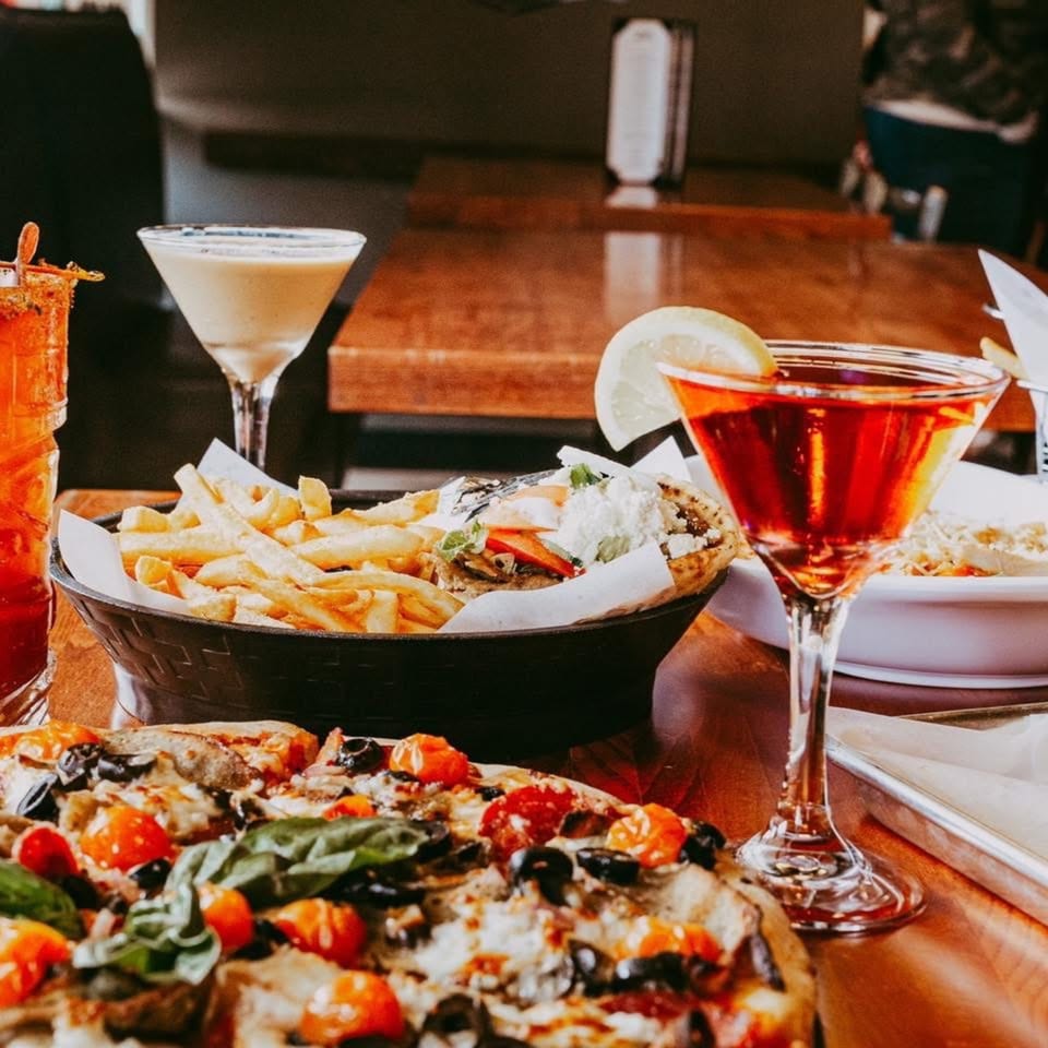 A table at Tito's Lounge with pizza, fries, a gyro, and three cocktails.