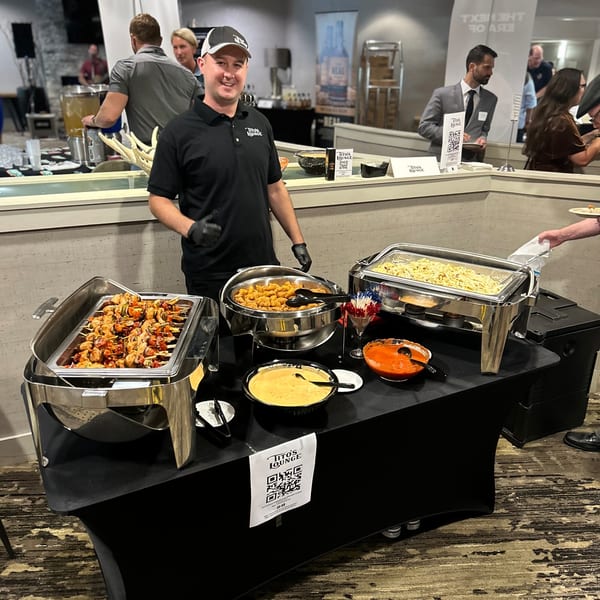 A Tito's Lounge staff member stands behind a buffet table with various bar-&-grill dishes.