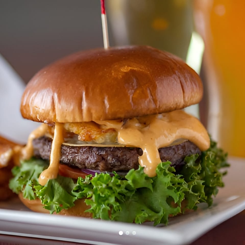 A close-up of Tito's Lounge burger with melted cheese, special sauce, lettuce, and tomato.